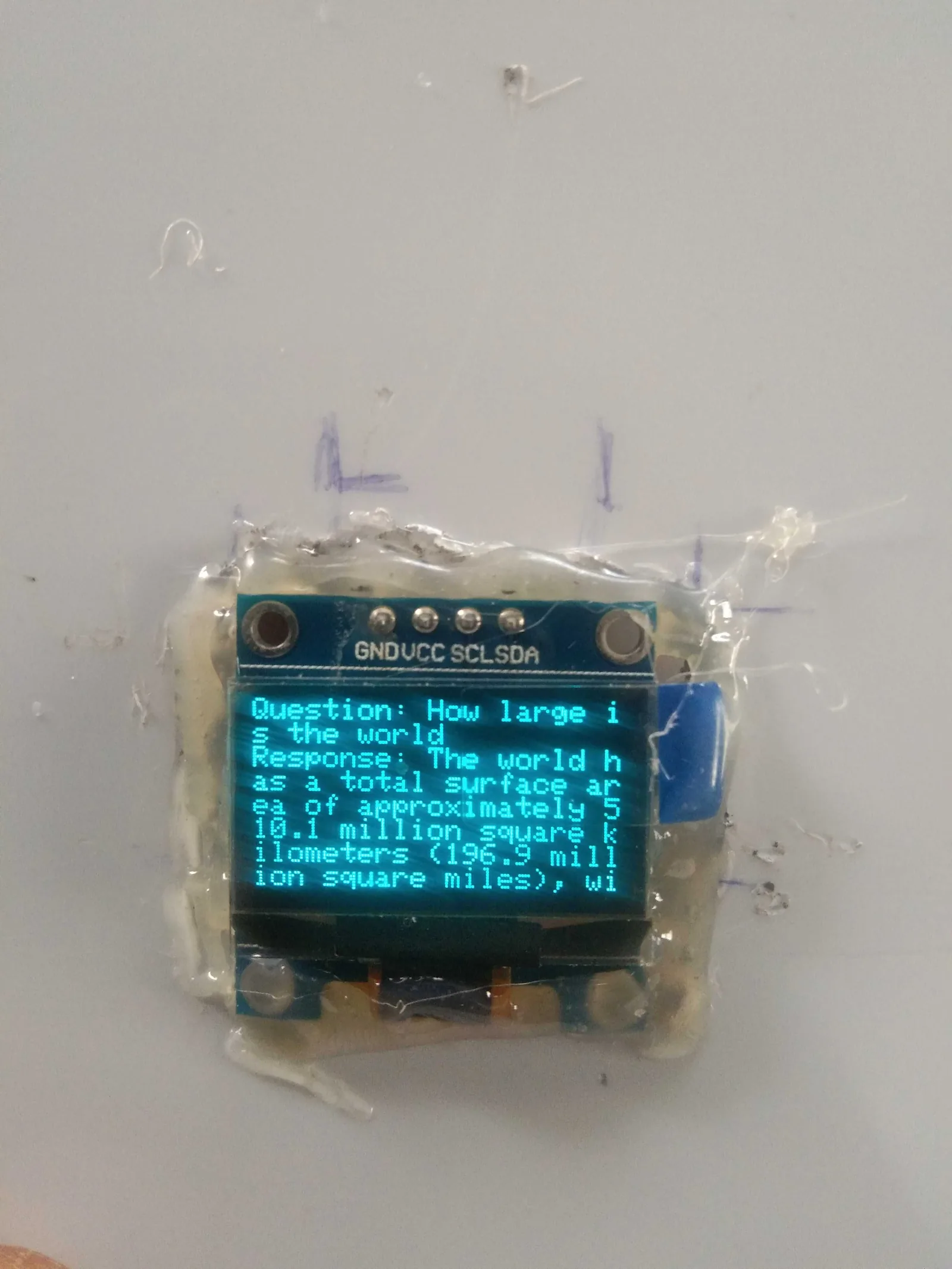 OLED display showing a question about the world's surface area and the assistant's answer